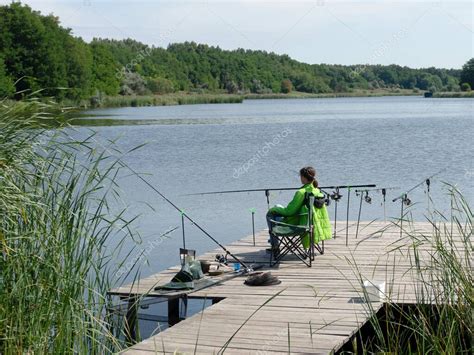 Chica de la pesca de la carpa en el hermoso lago azul con cañas de