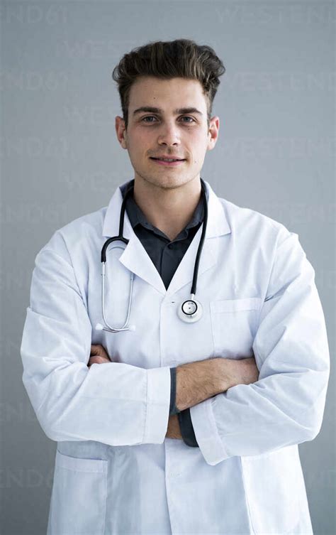 Male Handsome Doctor With Arms Crossed Against Gray Wall Stock Photo