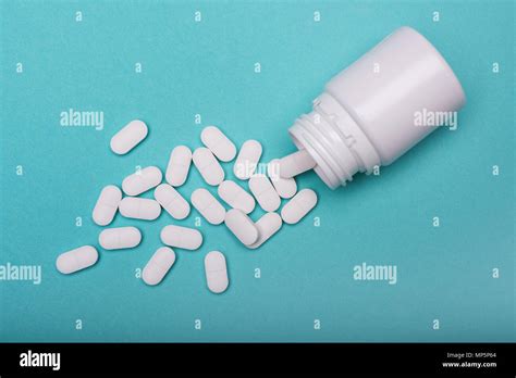 medication bottle and white pills spilled on blue pastel coloured background medication and