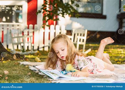 Cute Little Blond Girl Reading Book Outside On Grass Stock Photo