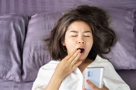 Premium Photo Tired Asian Woman Yawning In Bed Hand Holding Smart Phone