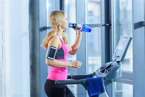 Blonde Woman Exercising On Treadmill And Drinking Water Stock Image