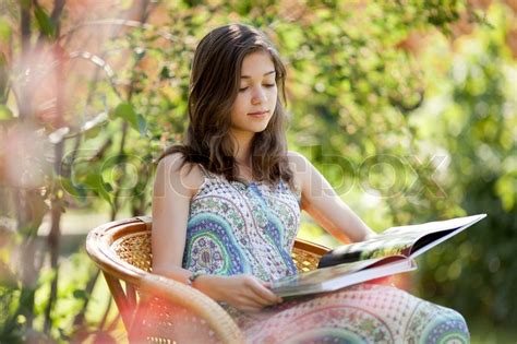 Girl Reading Book Sitting In Wicker Chair Outdoor In