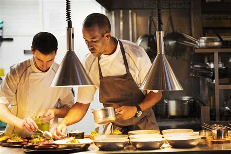 Two Chefs Standing In A Restaurant Kitchen Plating Food Stock Photo