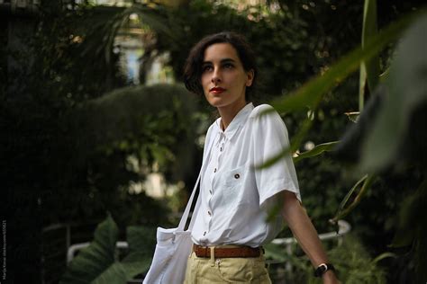 Woman In A White Shirt Standing In The Botanical Garden By Stocksy