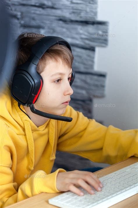 Teenage Boy In Headphones Uses Computer At Home At A Distance Learning