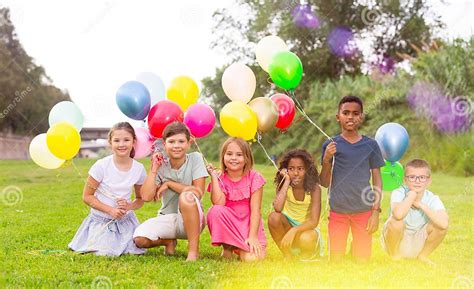 Happy Tweens With Balloons On Green Meadow In Summer Park Stock Photo