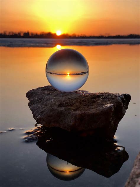 A Ball Sitting On Top Of A Rock In The Middle Of Water At Sunset Or Sunrise