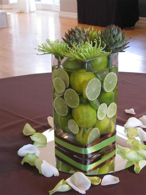 A Non Floral Centerpiece With A Vase Filled With Limes And Topped With