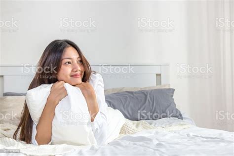 Portrait Of Smiling Relax Young Beautiful Asian Woman Lying On The Bed With Hugging White Pillow