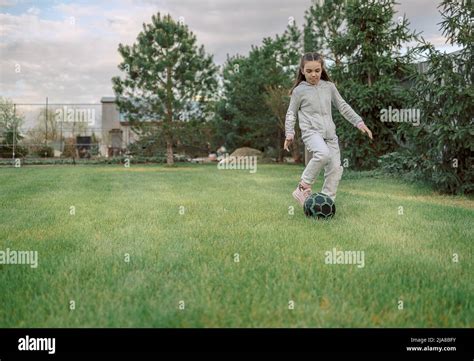 Cute Little Girl Playing Football With Soccer Ball On Green Lawn In