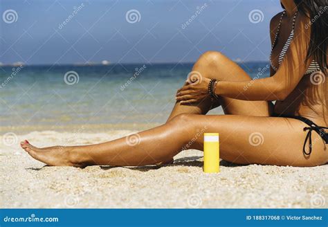 Tanned Woman Applying Sunblock Protection In Her Tanned Legs In A Paradise Beach Stock Photo