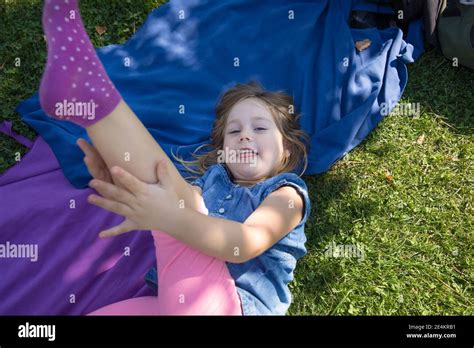 Four Years Old Blonde Girl Lying On Towels In The Green Grass Of Park