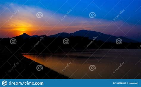 Sunset Landscape With Orange Sky Silhouettes Of Mountains And Lake