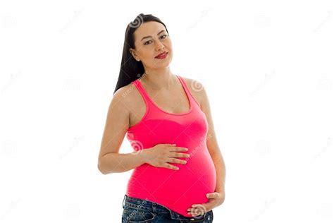 portrait of pregnant brunette touching her big belly and smiling on camera in pink shirt