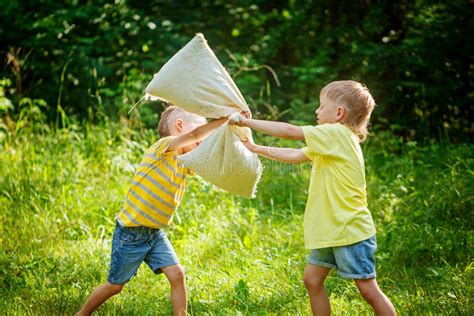 Children Fighting Together With Pillows In A Sunny Summer Garden Stock