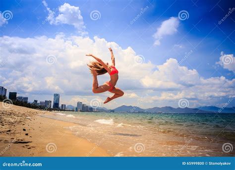 Blonde Slim Gymnast In Bikini In Jump Over Beach Against Sky Stock