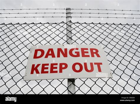 Danger Keep Out Sign On A Chain Link Fence Topped With Barbed Wire