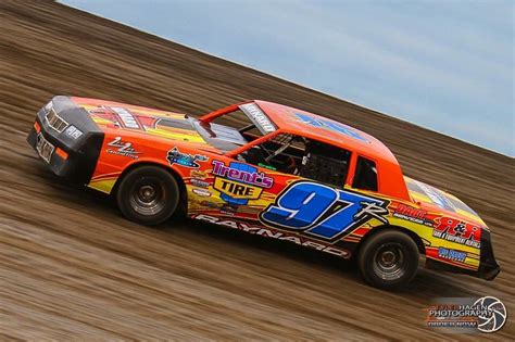 An Orange And Yellow Race Car Driving Down A Dirt Track With The Number