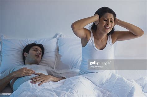 Man Snoring With His Wife Covering Ears With Hands On The Bed High Res