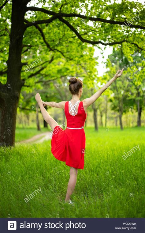 Slim Beautiful Brunette Girl In A Red Dress Performs Yoga Poses In A Summer Park Green Forest