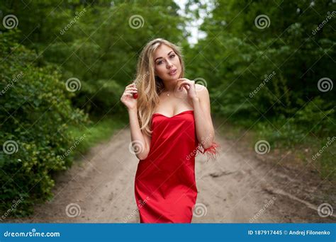 Beautiful Young Long Haired Blonde In A Red Dress Posing On The Road In A Summer Park With A