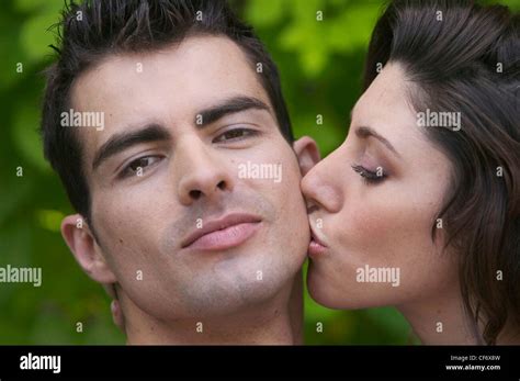 profile of female on right brunette hair kissing cheek of male on left short brown hair looking