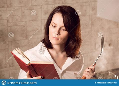 Beautiful Young Redhead Woman Reading A Book While Cooking On Kitchen