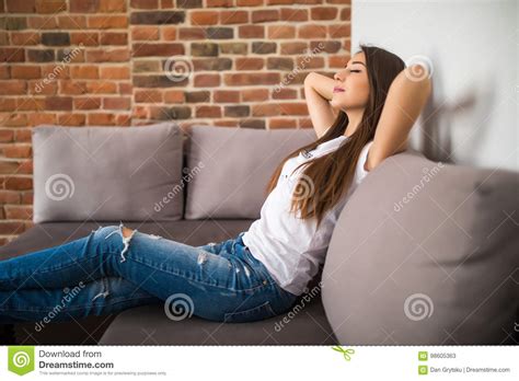 Smiling Young Woman Lying On Sofa At Hands Over Head Closed Eyes Stock