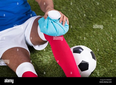 Close Up Of An Injured Male Soccer Player Applying Ice Pack On Knee