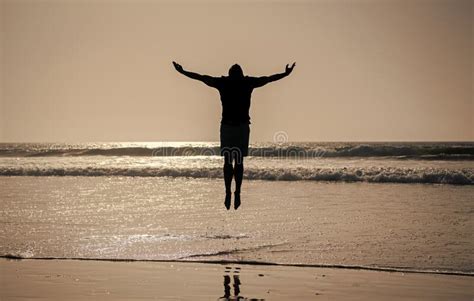 Silhouette Of Athletic Man Jump With Raised Hands On Summer Beach