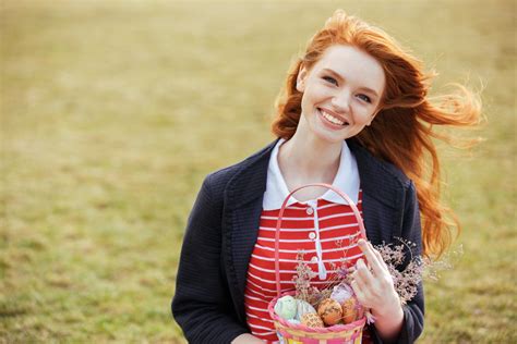 portrait of a smiling red head girl with long hair holding easter picnic basket with eggs and