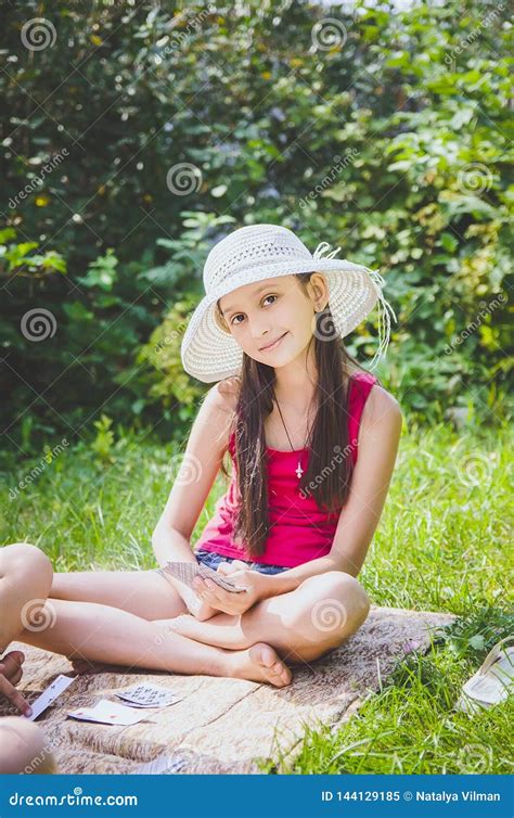 Beautiful Girl 10 Years Old In A White Hat Sitting On The Grass In The