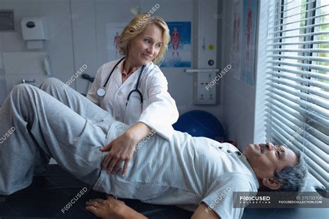 front view of caucasian female doctor examining senior mixed race male patient back in hospital