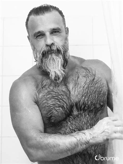 A Man With A Beard And No Shirt Is Standing In The Shower Holding His