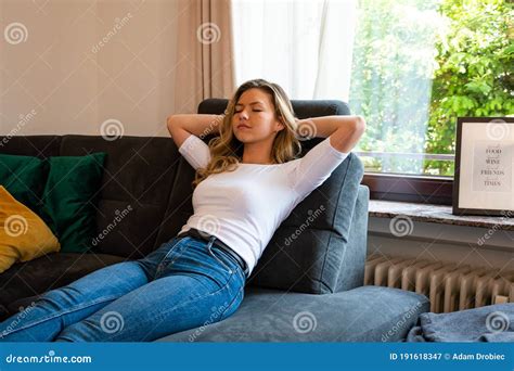 Young Woman Relaxing On Sofa Recliner With Eyes Closed And Hands Behind