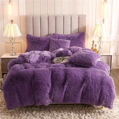 A Bed With Purple Comforter And Pillows On Top Of It In A Room Next To