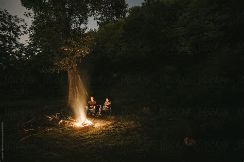Couple Sitting Beside A Campfire In The Forest At Night By Stocksy