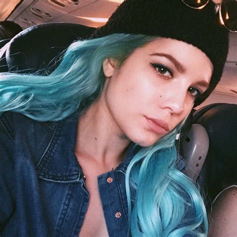 a woman with blue and green hair sitting in a car wearing a black beanie