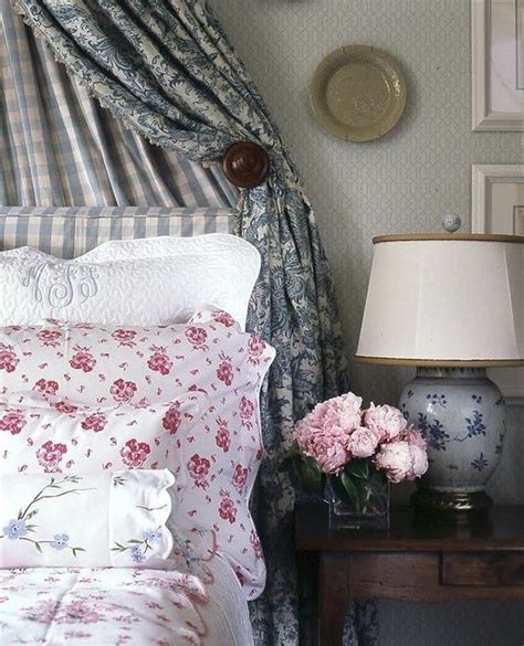 A Bed With Pink Flowers On It Next To A Night Stand And Lamp In The Corner