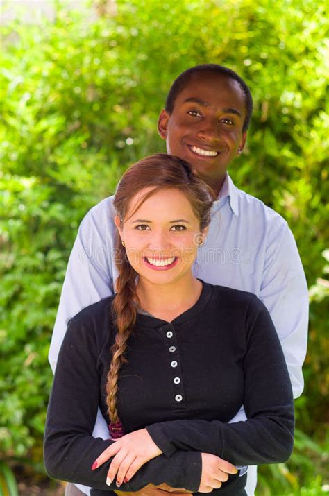 Beautiful Young Interracial Couple In Garden Environment Embracing And Smiling Happily To