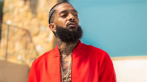 Nipsey Hussle Is Looking Side And Wearing Red Coat And Having Tattoos