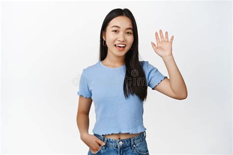 Friendly Asian Teen Girl Saying Hi Waving Raised Hand And Smiling