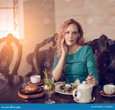 Young Beautiful Woman Is Sitting At The Table And Having Dinner In The