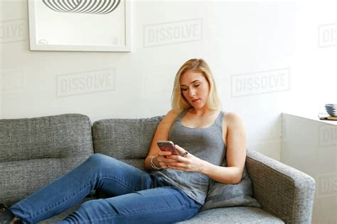 Caucasian Woman Sitting On Sofa Texting On Cell Phone Stock Photo