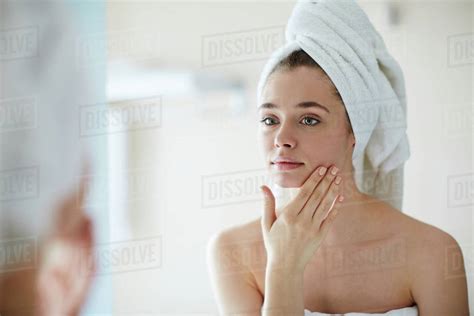 Young Woman Looking At Mirror In Bathroom And Pampering Her Face