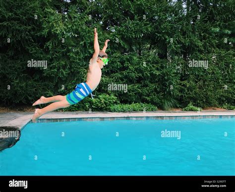 A Young Boy Jumping Into An Outdoor Swimming Pool During Summertime