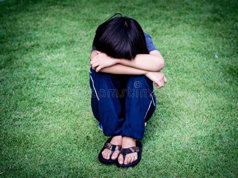 Little Boy Unhappy Sad And Sitting Alone On The Grass Field Stock Image