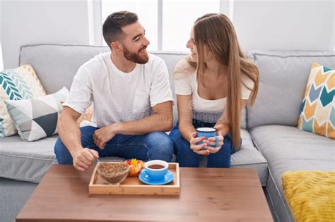 Man And Woman Couple Having Breakfast Sitting On Sofa At Home Stock