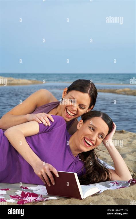 Two Young Women On Beach One Is Reading To The Other Smiling Sea And Sky In Background Stock